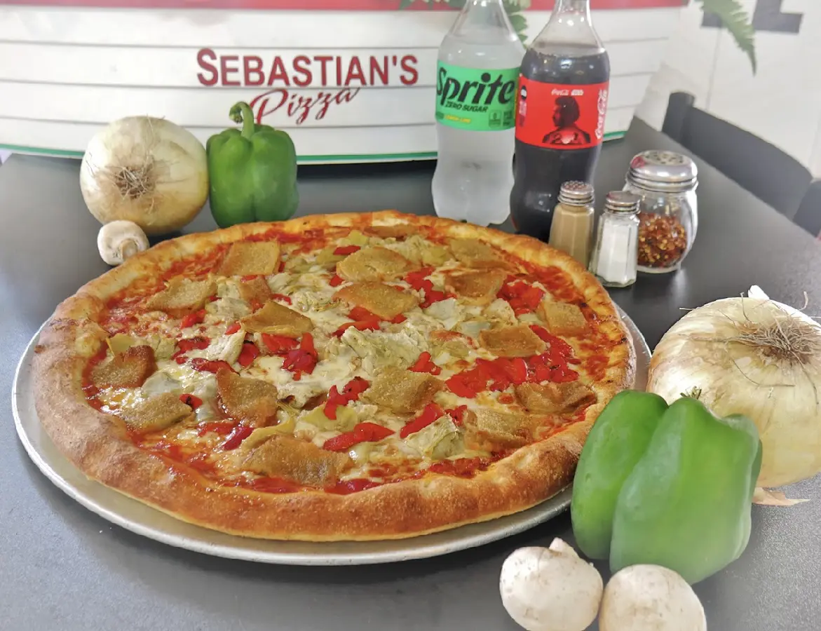 A freshly baked pizza with green and red bell peppers on a wooden table.