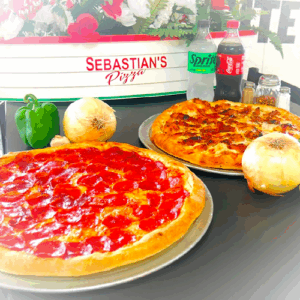 Two large pizzas with onions, green pepper, and soda on a table at Sebastian's Pizzeria.