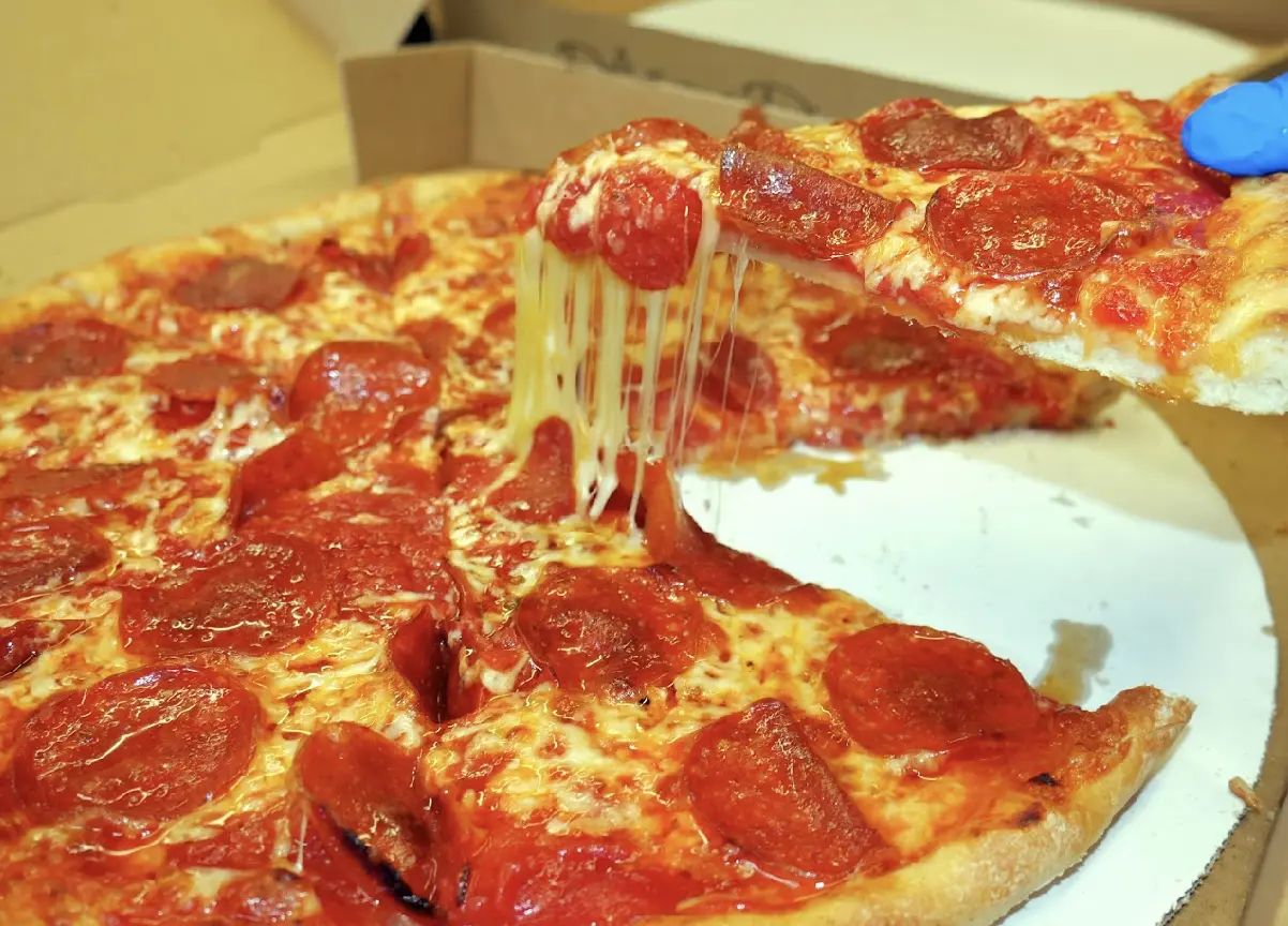 A slice of pepperoni pizza being lifted with melted cheese stretching.