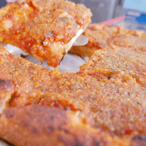 A slice of cheesy pizza being lifted from a whole pizza.