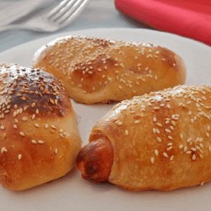 Three sesame seed-topped sausage rolls on a plate.